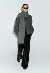 Cardigan oversize grigio in misto lana con colletto alto e chiusure a toggle, abbinato a pantaloni in velluto nero a gamba larga e occhiali da sole.