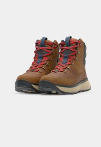 Bottes de randonnée en cuir marron avec des lacets rouges et bleus, semelles en caoutchouc et un col rembourré gris. Design durable pour une utilisation en extérieur.