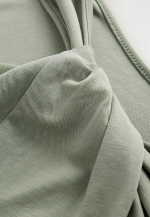 Zelená látka s hladkým povrchom, ktorá má dizajn skrúteného uzla a zhromaždené detaily na jednej strane. Mäkký a ľahký materiál.