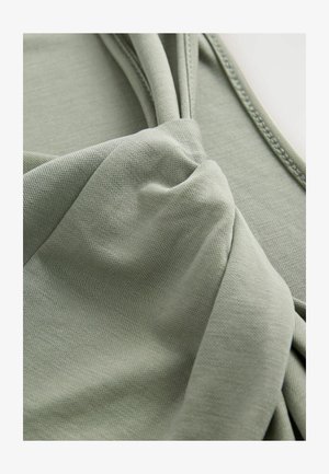 Tessuto verde con una superficie liscia, caratterizzato da un design a nodo ritorto e dettagli arricciati su un lato. Materiale morbido e leggero.