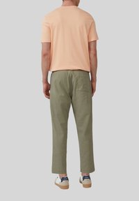 Heren T-shirt met korte mouwen in perzik, lichte stof; gecombineerd met olijfgroene broek, tapere fit, zijzakken en achterzak. Witte sneakers met blauwe accenten.