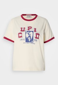 Κοντομάνικο κρεμ T-shirt με κόκκινο πλεκτό γιακά και μανίκια, με μπλε γραφικό σχέδιο που έχει το κείμενο "Cupid Lucky You Aim for a Cowboy."