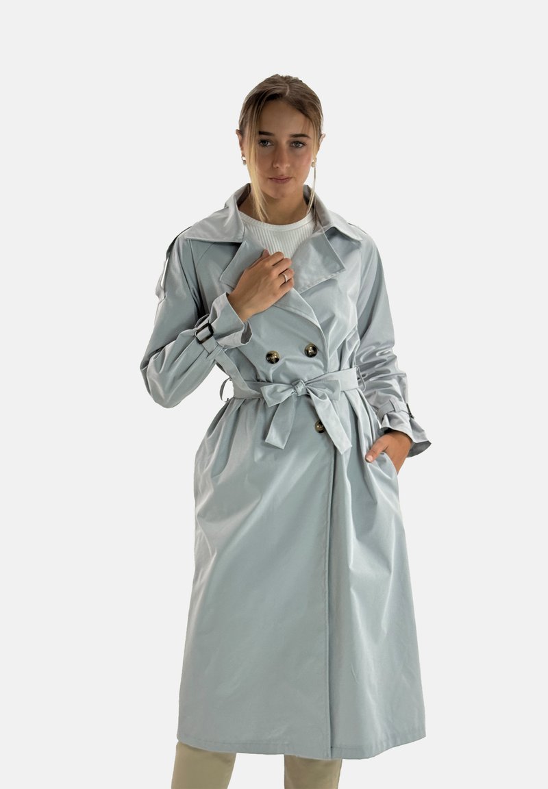 Ljusblå trenchcoat med dubbelknäppt design, guldknappar och bälte i midjan. Har en bred krage och långa ärmar.