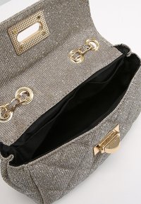 Metaliczna złota torebka pleciona o pikowanej strukturze. Posiada złote akcesoria i magnesowe zapięcie, a wnętrze wykończone jest czarną podszewką.