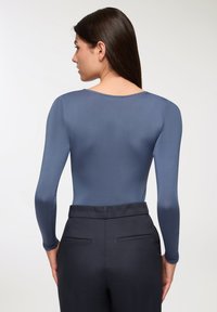 Body z długim rękawem w kolorze niebieskoszarym, charakteryzujące się gładką teksturą i okrągłym dekoltem, zestawione z ciemnymi, dopasowanymi spodniami. Minimalistyczne detale.