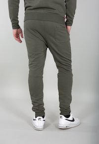Pantaloni jogger verde oliva con un design aderente, vita a coste e una tasca posteriore singola, abbinati a sneakers bianche con dettagli neri.