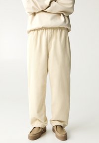 Lichtbeige ribbelstof broek met een elastische tailleband, met een losse pasvorm en taps toelopend ontwerp, gecombineerd met lichtbruine schoenen.
