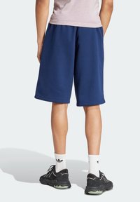 Námořnické modré teplákové šortky z měkké tkaniny, s elastickým pasem a volným střihem, v kombinaci s černými teniskami a bílými ponožkami po kotníky.