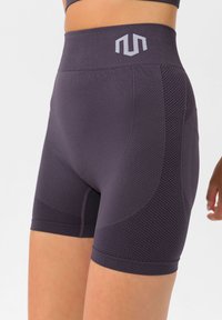 Dunkelpfolgenfarbene Sportshorts mit strukturierten Netzpaneelen, hohem Bund und Logodetails auf der Vorderseite. Glattes Material und figurbetontes Design.