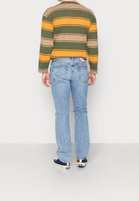 Randig långärmad skjorta med gröna, gula och bruna ränder; blå denimjeans; canvas sneakers med marinblå och beige accenter.