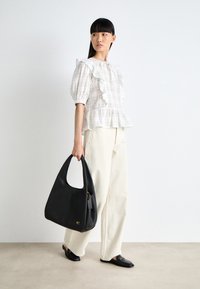 Μαύρη δερμάτινη τσάντα hobo με λεία υφή και χρυσά αξεσουάρ, συνδυασμένη με ένα ανοιχτόχρωμο, καρεδάτο τοπ peplum και φαρδιά, εκρού παντελόνια.