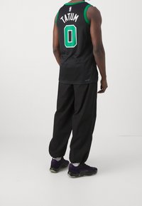 Maglia da basket senza maniche nera con accenti verdi, con "TATUM" e il numero "0" sul retro; indossata con pantaloni neri larghi e sneakers viola.