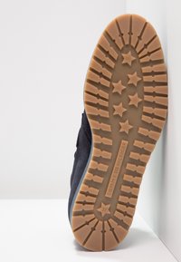 Mörkblå sneaker med en flat, strukturerad gummisula med stjärn- och pilmönster; tillverkad av ett mjukt mockaliknande material.