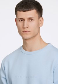 Sudadera azul claro con cuello redondo y texto en relieve "LINDBERGH" en el pecho. Fabricada con un tejido suave y liso.