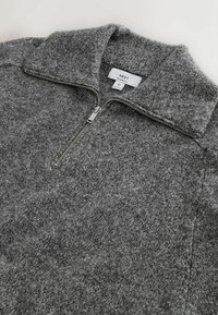 Harmaa fliispulloveri, jossa on neljänneksen vetoketju edessä, korkea kaulus ja pehmeä koostumus. Merkissä lukee merkki 'NEXT' ja koko 'M'.