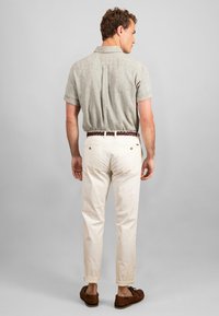 Cămașă scurtă de culoare verde deschis, cu pliuri la spate, asociată cu pantaloni albi din bumbac și o curea împletită maro, purtată cu pantofi maro.