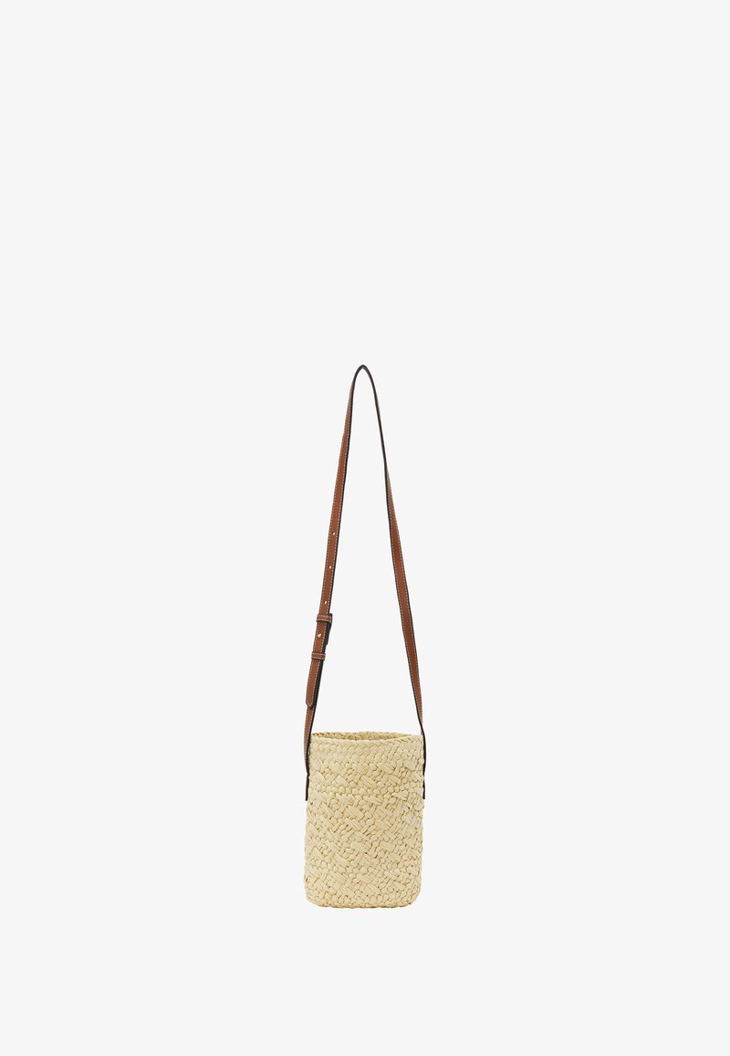 Woven straw crossbody bag in light beige with a brown adjustable leather strap. Cylindrical shape, textured surface, and open top design.