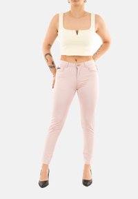 Jeans skinny de color rosa claro combinados con una blusa corta de canalé blanca con escote cuadrado y un pequeño detalle recortado. Tacones altos negros.