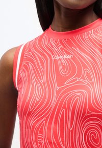 Κόκκινο τοπ χωρίς μανίκια με λευκό αφηρημένο σγουρό μοτίβο και λογότυπο Calvin Klein, φορεμένο από άτομο με σκουρόχρωμη επιδερμίδα και ίσια σκούρα μαλλιά.