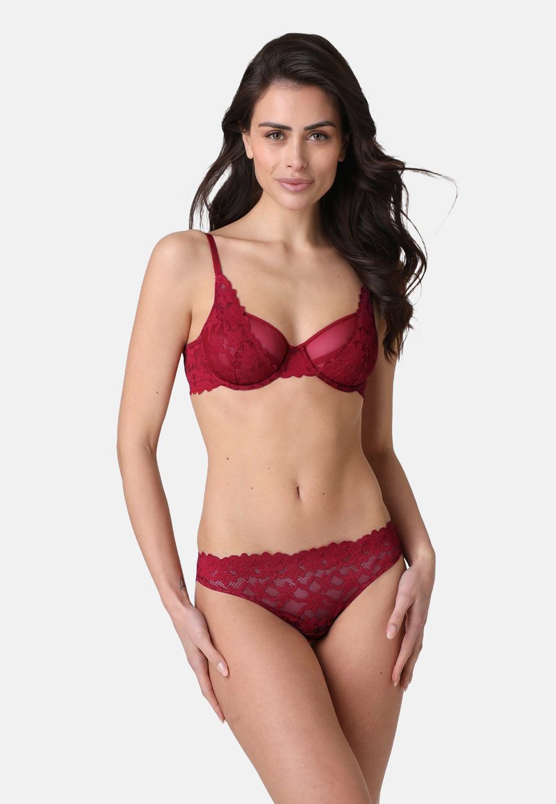 Set di lingerie in pizzo rosso che comprende un reggiseno con pannelli trasparenti e dettagli floreali, abbinato a mutande in pizzo coordinate. Design texturizzato e delicato.