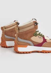 Zapatillas altas de ante marrón con acentos texturizados en gris y beige, suela blanca y naranja, y un forro de felpa. Incluye cordones multicolores.