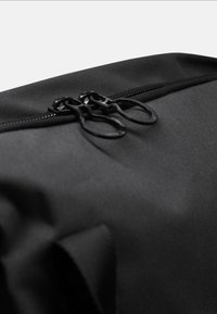 Borsa in tessuto nero con superficie testurizzata. Presenta due zip nere nella parte superiore, evidenziando un design senza soluzione di continuità.