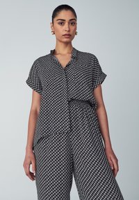 Zwart-wit gestreept bovenstuk met korte mouwen en een ontspannen pasvorm. Soepele textuur met een kraag en sluiting met knopen aan de voorkant. Gestyled met bijpassende broeken.