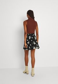 Top senza maniche marrone abbinato a una gonna nera floreale, caratterizzata da un design svasato e stivaletti crema con tacco a blocco.