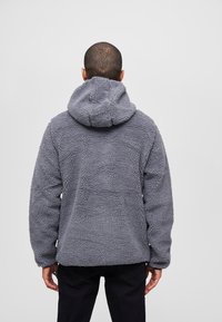 Gray fleece jacket with a textured, fluffy surface, featuring a hood and long sleeves, viewed from the back against a plain backdrop.