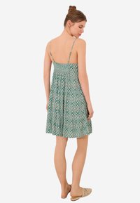 Robe d'été verte à motifs avec des fines bretelles, un corsage froncé et une jupe évasée. Présente un design géométrique avec des couleurs contrastées.