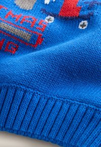 Pulover tricotat albastru cu tiv zimțat, având un design tematic de vacanță în culorile roșu, gri și alb, care prezintă diverse modele jucăușe.
