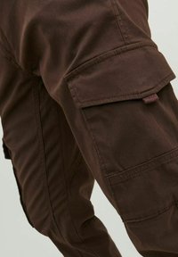Pantaloni cargo marroni con tasche laterali, dettagli cuciti e tessuto leggermente strutturato. Il design è pratico e funzionale.