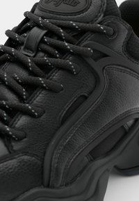 Svart sneaker med texturerat lädermaterial, kontrasterande snören med blå detaljer och en tjock gummisula med en intrikat design.