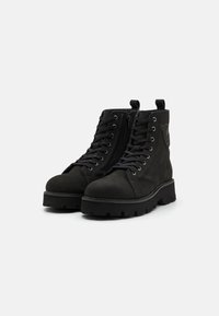 Bottines en suede noir avec un bout rond, un laçage à l'avant et une fermeture éclair sur le côté, présentant une semelle texturée et un détail de logo subtil.