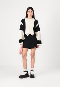 Svart og hvit ribbestrikket oversized genser med lange ermer, kombinert med et svart skjørt og en rosa veske. Kraftige svarte sko med hvite sokker.