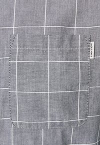 Grijs geruit shirtstof met een wit rasterpatroon, voorzien van een enkele borstzak en een klein label met de tekst "JACK & JONES".