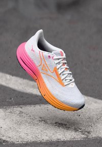 Løbesko med en hvid overdel og en gradient sål i orange og pink, tekstureret stof og fremtrædende snøresystem.