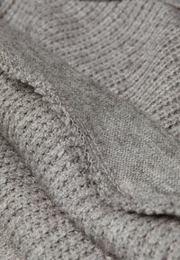 Un tissu en tricot gris avec un motif texturé est superposé à un matériau gris lisse et plus épais, mettant en valeur de fines coutures et de subtiles variations.