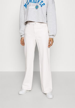 Personne portant un pantalon large blanc, des baskets blanches et un sweat court gris avec le texte bleu "Milwaukee Wisconsin".