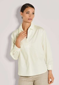 Helles gelbes Hemd mit Kragen, langen Ärmeln und lockerer Passform, aus glattem Stoff gefertigt. Verfügt über eine einzelne Brusttasche.