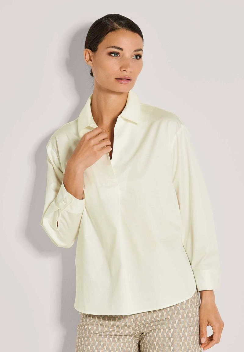 Helles gelbes Hemd mit Kragen, langen Ärmeln und lockerer Passform, aus glattem Stoff gefertigt. Verfügt über eine einzelne Brusttasche.