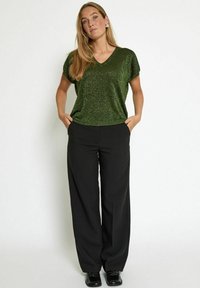 Zeleni svetlucavi top z v-neck izrezom, uparen s črnimi širokimi hlačami. Top ima sproščen kroj, medtem ko imajo hlače sprednje žepe.