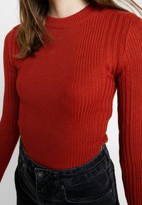 Gestreepte rode trui met een ronde hals en lange mouwen, gecombineerd met hoge zwarte corduroy broek, wat een slanke silhouet laat zien.