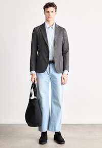 Γκρι σακάκι με δύο μπροστινές τσέπες, ανοιχτό μπλε ριγέ πουκάμισο, ανοιχτό μπλε τζιν με φαρδιά μπατζάκια, μαύρη τσάντα και μαύρα μποτάκια μέχρι τον αστράγαλο.