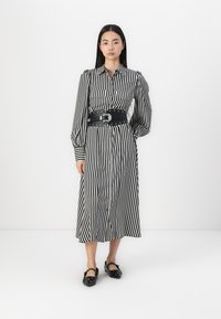 Φόρεμα με λευκές και μαύρες ρίγες, με κουμπιά μπροστά, μακριά μανίκια και εφαρμοστό μαύρο ζώνη. Συνδυασμένο με μαύρες φλατ παπούτσια με τρουκς.