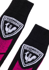 Chaussettes noires et roses avec des poignets côtelés, arborant un logo blanc de Rossignol représentant un coq à l'intérieur d'un écusson à l'avant.