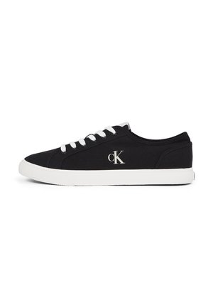 Baskets basses noires avec semelle blanche et lacets blancs, comportant le logo "cK" sur le côté, affichées sur fond blanc.
