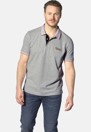 Graues Polohemd mit kontrastierendem Kragen in Schwarz und orangefarbenen Akzenten. "TEAM 1914" auf der Brust gestickt. Getragen mit blauen Jeans.