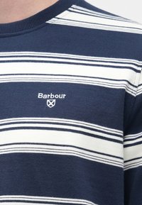 Sötétkék csíkos pulóver, puha anyagból készült, fehér vízszintes csíkokkal és kis fehér "Barbour" logóval a mellen.