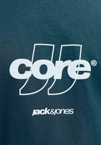 Sötétzöld pamut póló vastag, fehér "core" és "jack & jones" felirattal. Finom, sima anyagból készült, klasszikus kerek nyakkivágással.